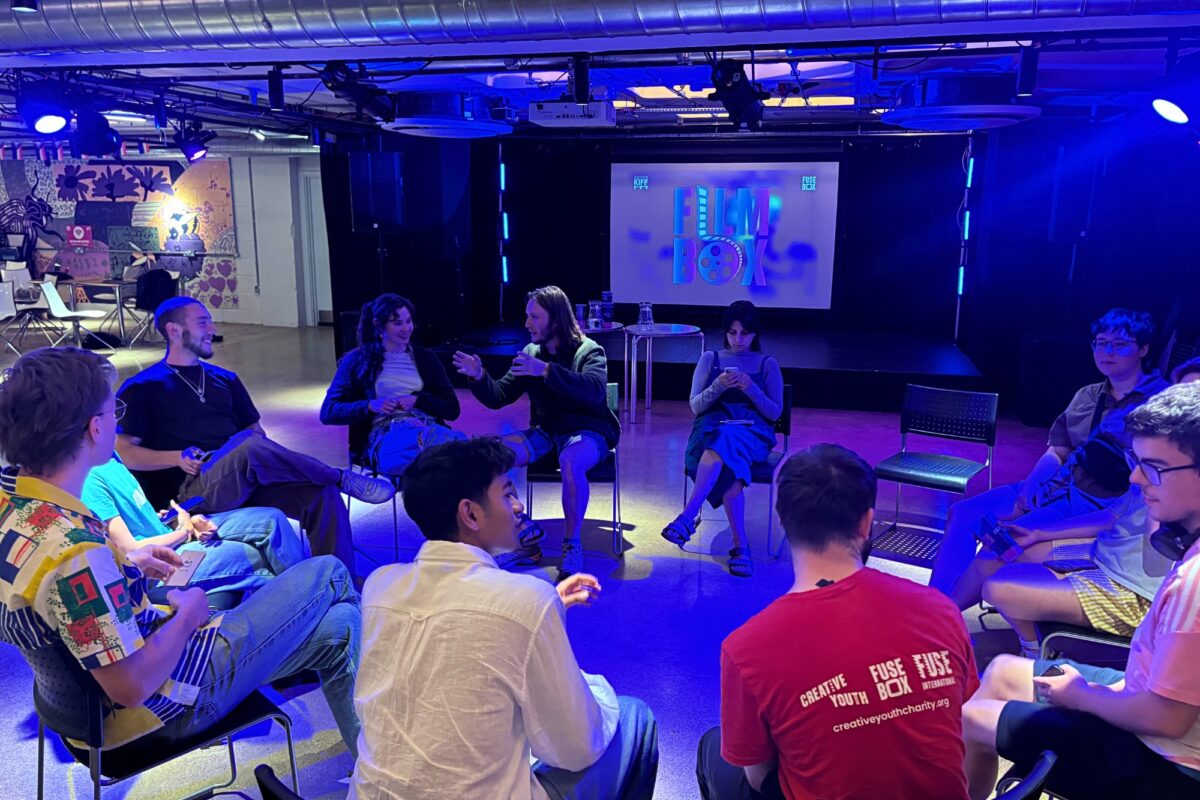 young people sit in a circle facing a screen