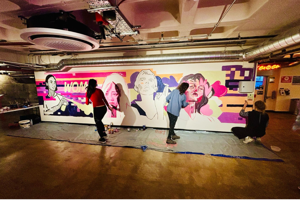 two artists work on a in-progress mural of faces